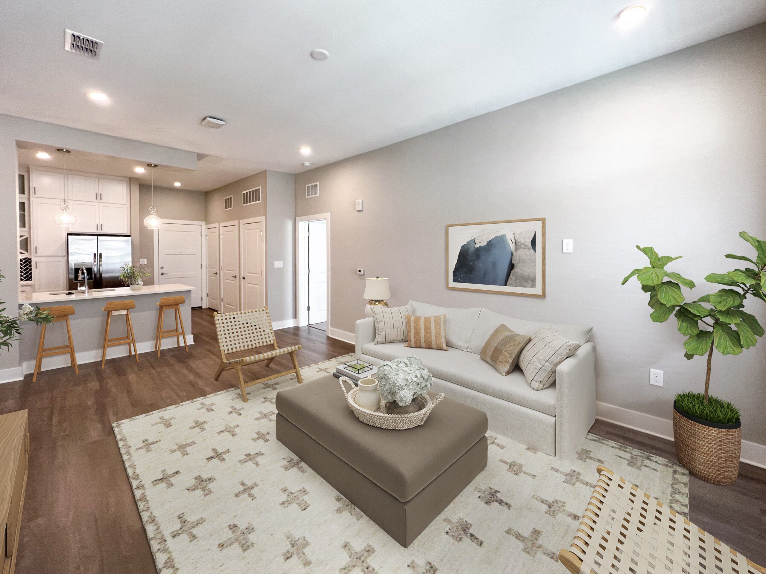 A modern Northwood Ravin living room with a light gray sofa, a patterned rug, two wooden chairs, a central ottoman, and an open kitchen in the background featuring bar stools and pendant lighting.