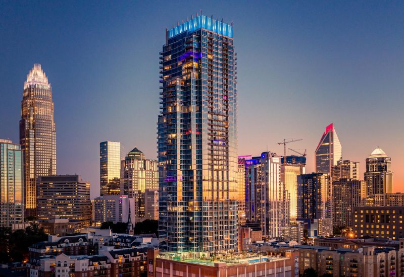 A city skyline at dusk featuring illuminated high-rise buildings, with a prominent modern skyscraper in the center surrounded by other towers and structures, reminiscent of Northwood Ravin's architectural elegance.