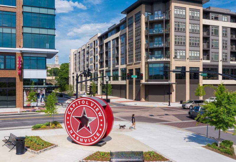 Northwood Ravin Property Management Portfolio, RESIDENCES AT CAPITOL VIEW in Nashville, TN, multi-family, multi-story apartments showing the building exterior with plentiful windows, green trees, and retail shops on the first floor