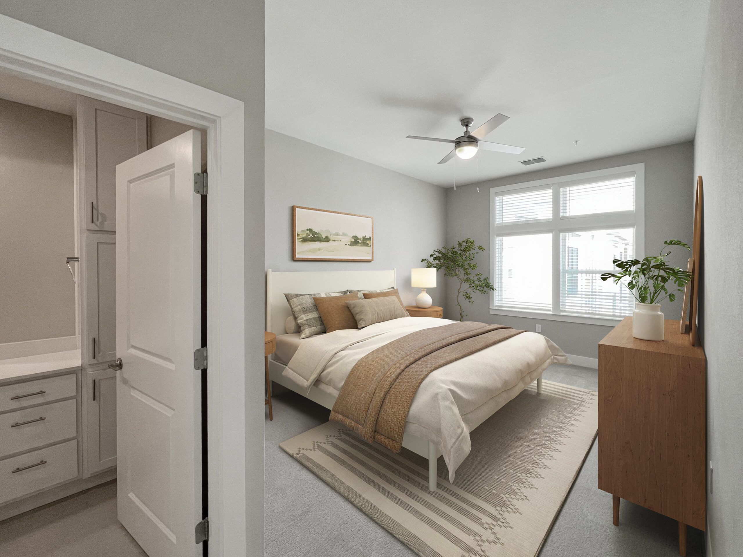 A bright Northwood Ravin bedroom with a double bed, beige bedding, wooden dresser, indoor plant, painting on the wall, ceiling fan, and an attached bathroom visible through an open door.